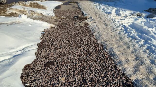 Closeup gravel path bordered by snow. Small stones and salt create gritty textured surface along pedestrian road during winter.