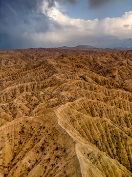Aerial view of the dramatic eroded ridges and deep gullies of Kan'on Aksay under a stormy sky with light breaking through the clouds in Ak Say, Issyk-Kul Region, Kyrgyzstan.