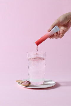 Hand Adding Pink Powder to Glass of Water on Minimal Pink Background
