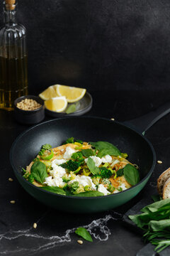 Omelette with broccoli, cheese, and herbs in frying pan