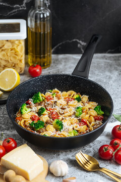 Orecchiette pasta with broccoli, tomatoes, and grated cheese in black 
