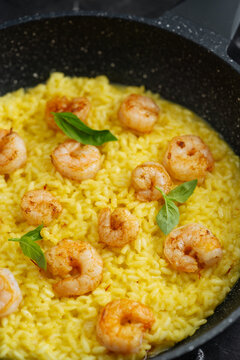 Close-up of saffron risotto with shrimp and basil in a frying pan