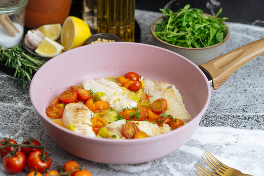 Cooked white fish fillets with cherry tomatoes and herbs in pink pan