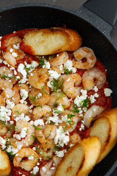 Shrimp with tomato sauce, feta cheese, herbs, and toasted bread in a f