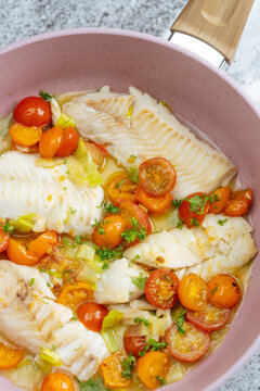 Cooked white fish fillets with cherry tomatoes, leeks, and herbs in a 