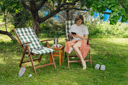 Woman reading in garden with coffee and badminton set nearby