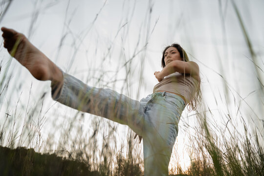 Woman dancing and moving in tall grass during sunset in a rural area