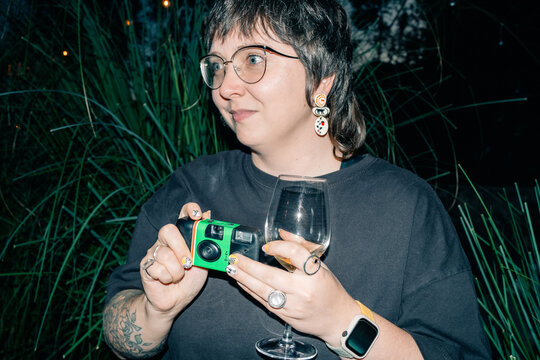 Woman Holding Camera and Wine Glass in Outdoor Setting