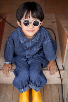 Chinese boy, wearing sunglasses and all geared up, sit on a porch