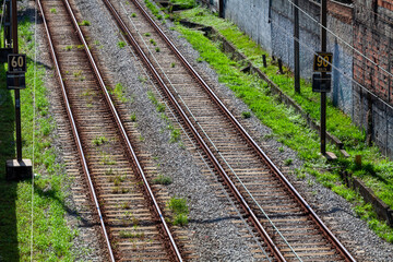 Fototapeta premium Railway tracks running through an urban area with visible speed limit signs, gravel ballast, and surrounding vegetation. Concept of transportation, infrastructure, logistics, and mobility.