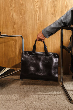 Hand holding leather briefcase near table with notebooks