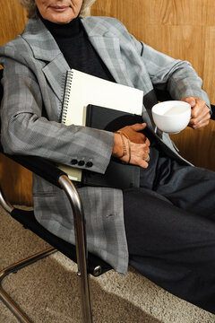Close-up of person holding coffee cup and notebooks in chair