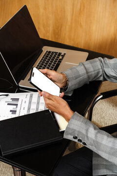 Businessperson using smartphone at desk with laptop and report