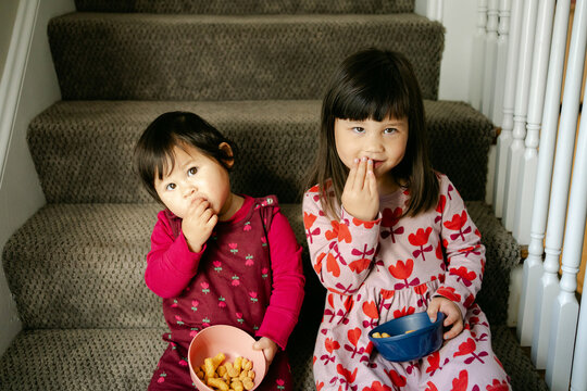 two little girls, sisters, eating snacks on the stairs 