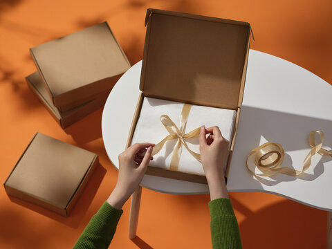 A person carefully ties a ribbon around a wrapped gift box
