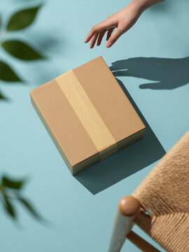 A hand reaching for a cardboard box on a turquoise surface.