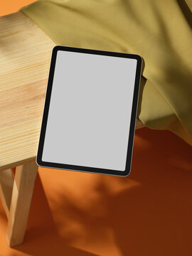 A modern iPad sits on a wooden table against an orange backdrop