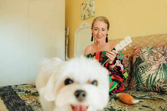 Small dog in foreground with woman playing ukulele