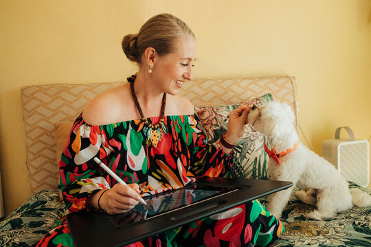 Woman feeding dog treat while working on tablet
