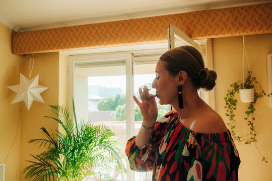 Woman playing musical whistle near window at home