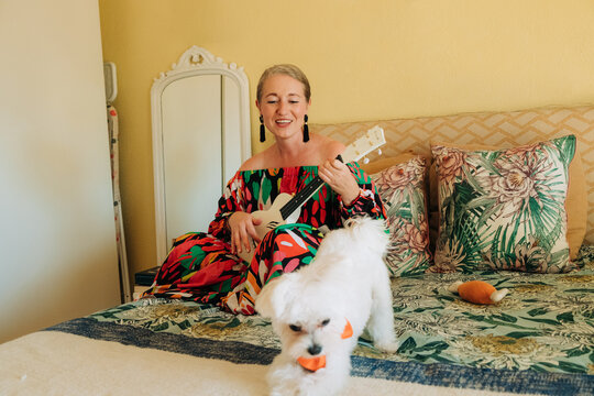 Smiling woman playing ukulele on bed at home