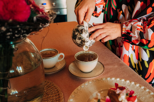 Woman pouring tea into cups during cozy home tea time
