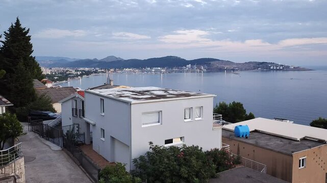 There are houses and trees on the high seashore, and a port is located in the bay. The street lights came on. On an autumn evening, the sun sank below the horizon and painted the sky and clouds