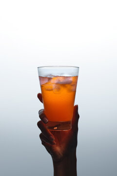 Hand holding a refreshing orange drink with ice cubes against grey