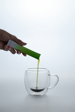 Green liquid being poured into a clear glass mug on a white background