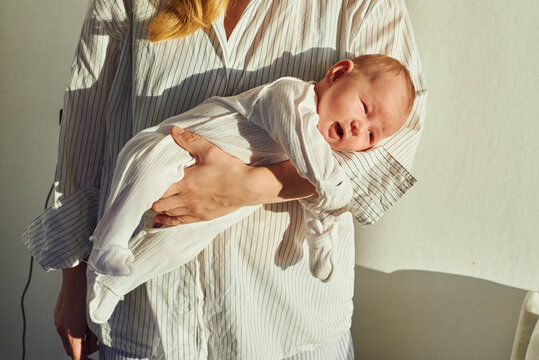 Mother holds newborn baby with soft sunlight in a warm indoor space