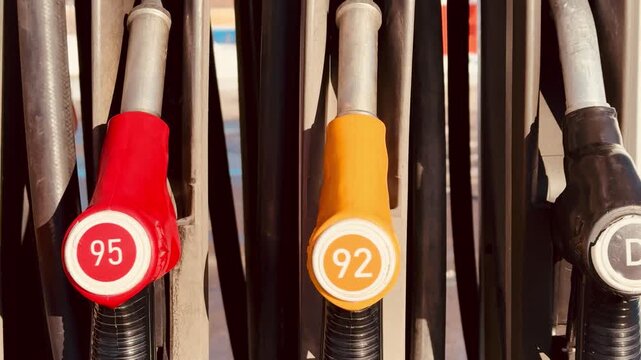 Closeup gas pump nozzles red yellow, octane labels and diesel marker, metal handles and rubber hoses, sunlight highlights textured.