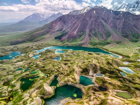 Aerial view of Tulpar Lake and turquoise alpine ponds nestled among rolling green hills with the snow-capped Pamir mountains in the background Alay District, Osh Region, Kyrgyzstan.