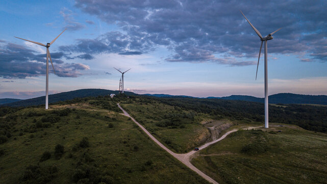 Wind turbines standing on rolling green hills under a dramatic sky 