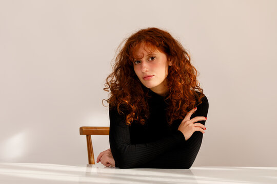 Young Woman With Curly Hair Sits at a Table in a Bright Room