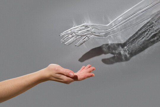 Human hand reaching to the transparent plastic hand sybol of AI