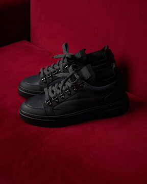 Black sneakers resting on a red couch