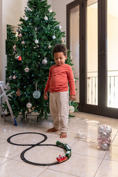 Child Plays With Train Set Near Christmas Tree in Home