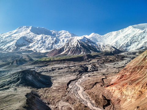 Aerial view of Puteshestvennikov Travellers Pass with snow-capped peaks and a winding riverbed under a clear blue sky Chong-Alay District, Osh Region, Kyrgyzstan.