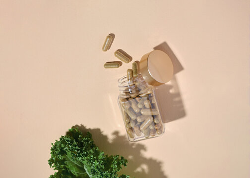 Capsules spill from a glass jar, complemented by fresh kale