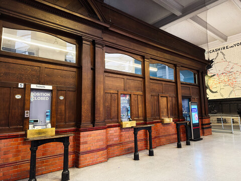 Vintage wooden ticket booth and cashier counter inside a historic train station in Manchester, UK with brick base and ornate paneling