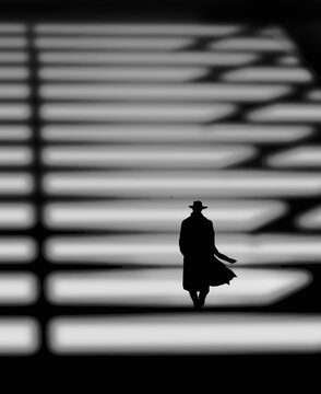 The mood iis dark, blustery, urban chill in this noir 3-d illustration of a man in an overcoat and hat walking at night in the shadows