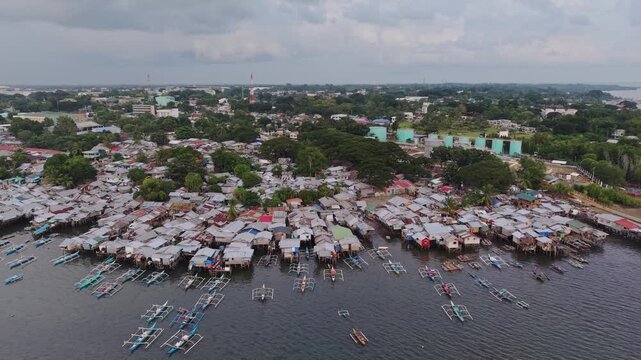 Backward aerial pull back above a dense coastal stilt home settlement on the shoreline of Puerto Princesa Bay in Palawan Philippines with bangka boats drifting on calm tropical water