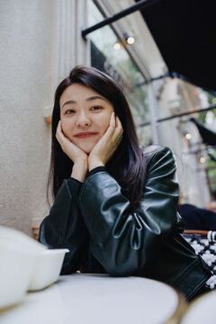 Smiling Woman Resting Chin on Hands at Outdoor Cafe