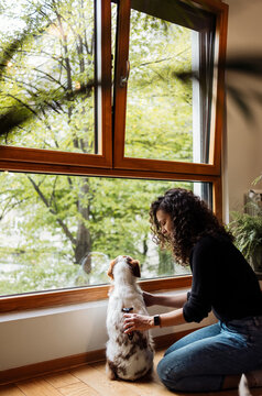 Woman Petting Dog by Window Looking Outside