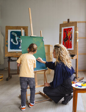Teacher Guides Child Painting In Art Studio