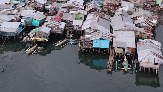 Aerial view of stilt homes with corrugated metal roofs standing above shallow tidal water and parked bangka boats in Puerto Princesa on the island of Palawan Philippines