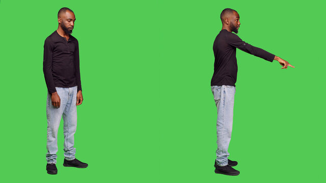 Confident adult pointing at the floor waving at someone, calling over to say they dropped something on camera. Young optimistic man with jeans and shirt over full body green screen.