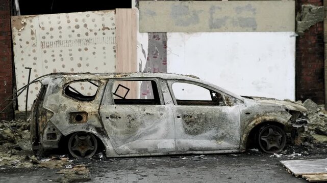 Burned out car wreck abandoned on city street. Destroyed vehicle after fire accident. Vehicle hulk as result of war conflict or arson. Urban catastrophe and property damage concept.