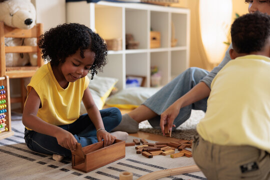 Children and adult play with wooden blocks on rug.