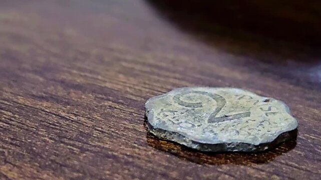 This weathered, scalloped-edge coin from India features a prominent "2" and the word "PAISE." Its dull, metallic surface shows significant wear, resting on a dark, textured wooden tabletop.